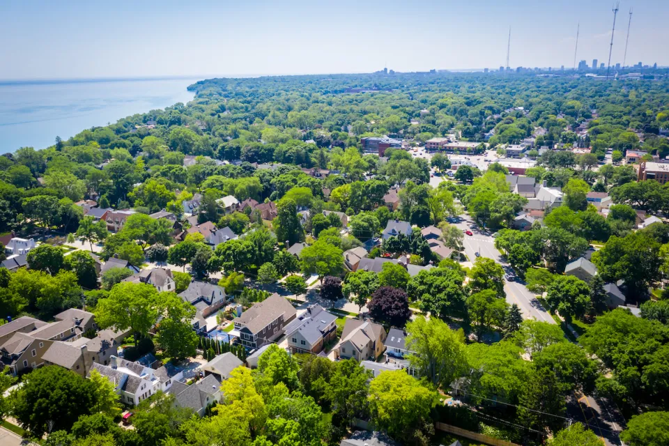 Aerial view of large homes surrounded by mature trees with Lake MIchigan shoreline at left.